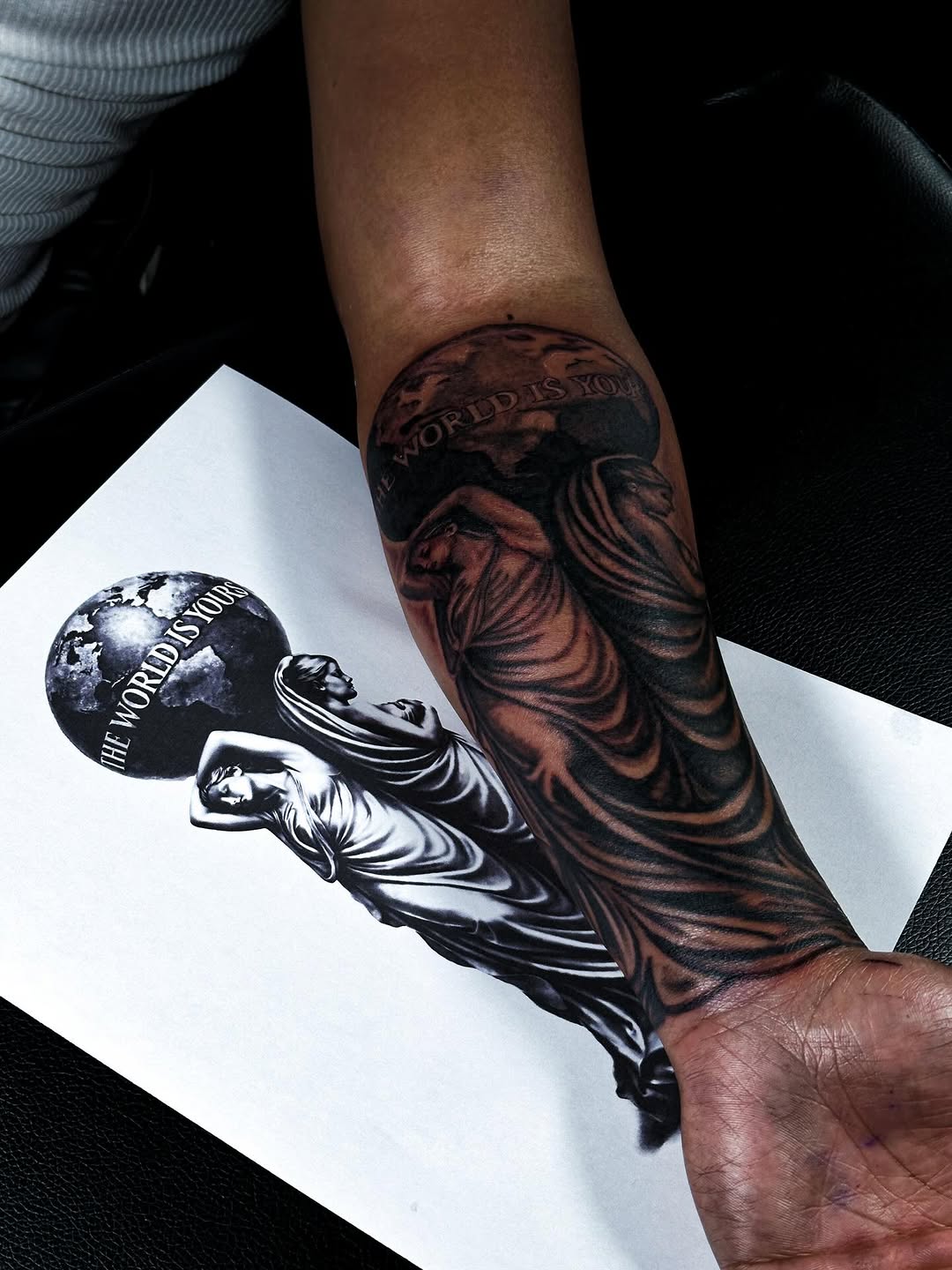 Monumental black-and-gray realism forearm tattoo, draped statue with globe