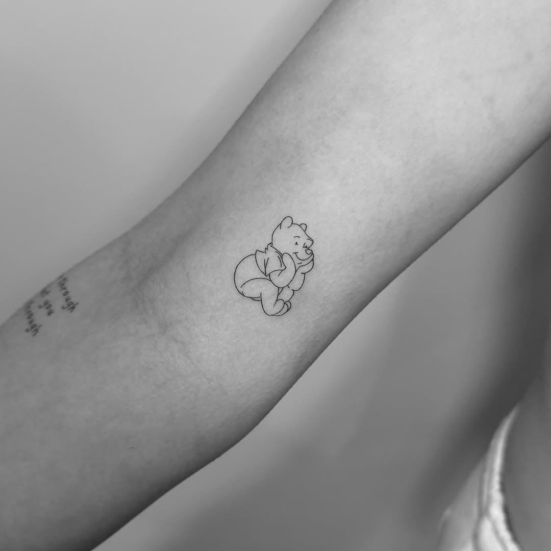 Minimal Winnie-the-Pooh line-art tattoo on forearm