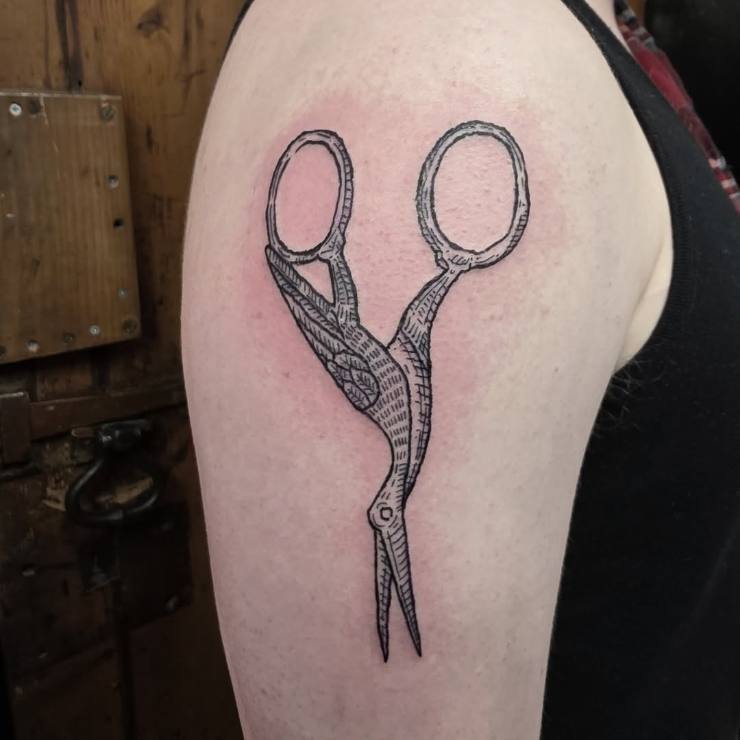 Embroidery-scissors silhouette in bold woodcut engraving linework.