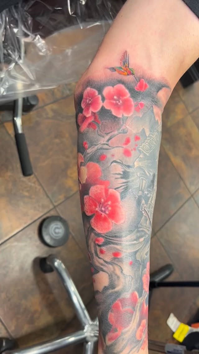 Vibrant cherry blossoms with a hummingbird on a grayscale Japanese sleeve.