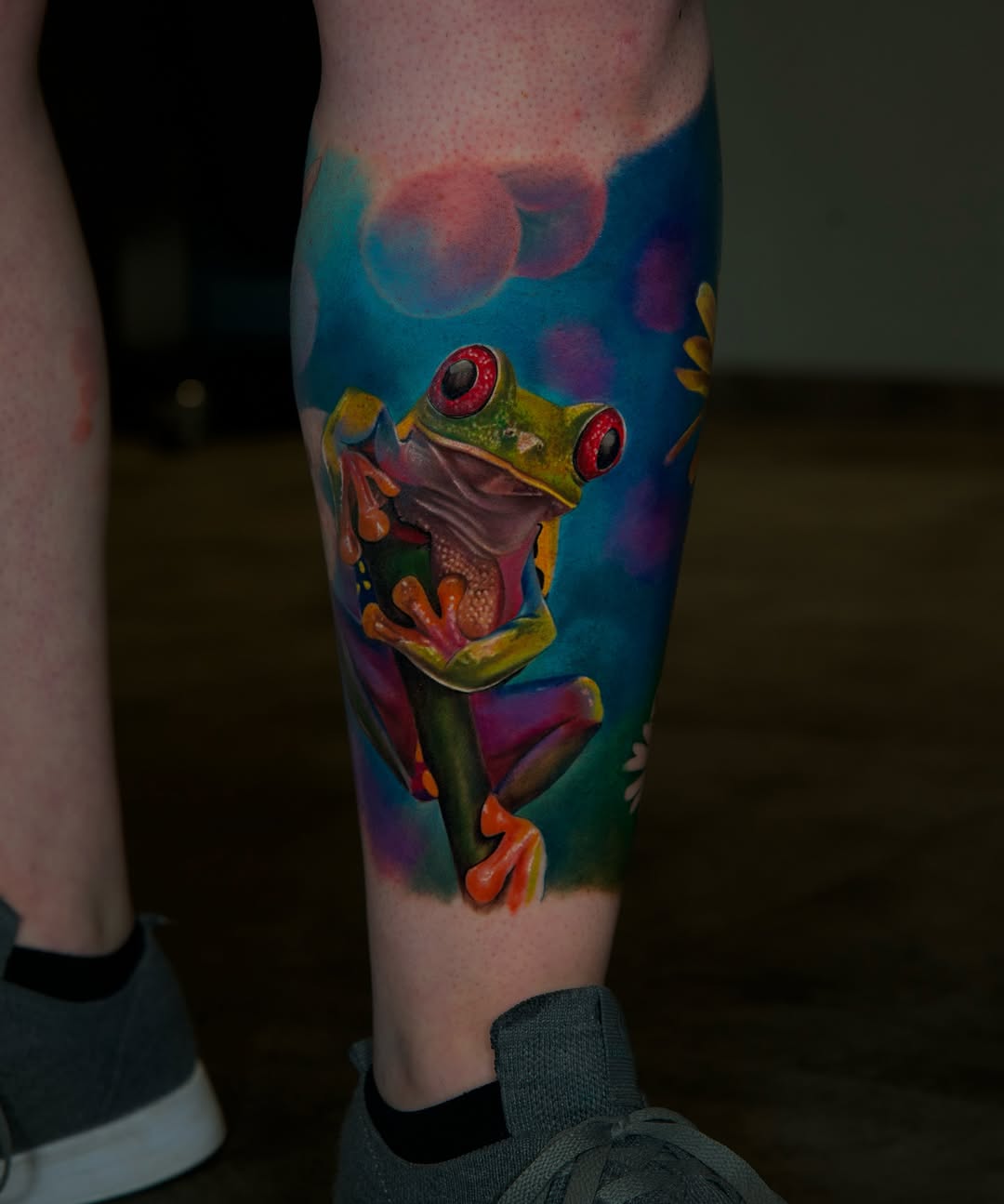 Vivid neon red-eyed tree frog on leg, bold background