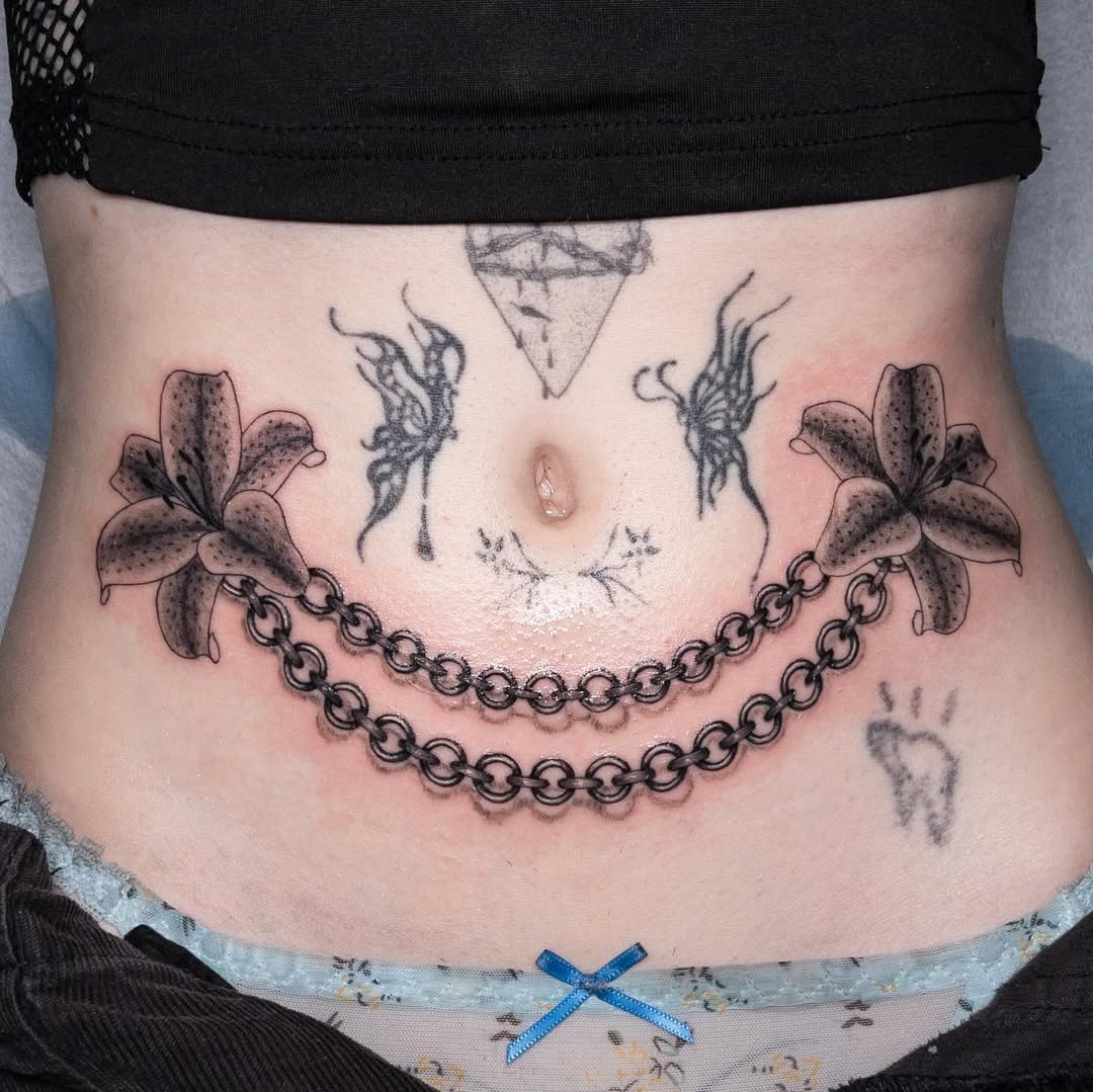 Floral lilies flank a chain-wrapped belly piece with central diamond.