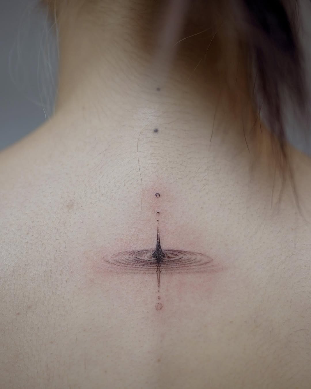 Minimalist water-drop ripple tattoo on the nape.
