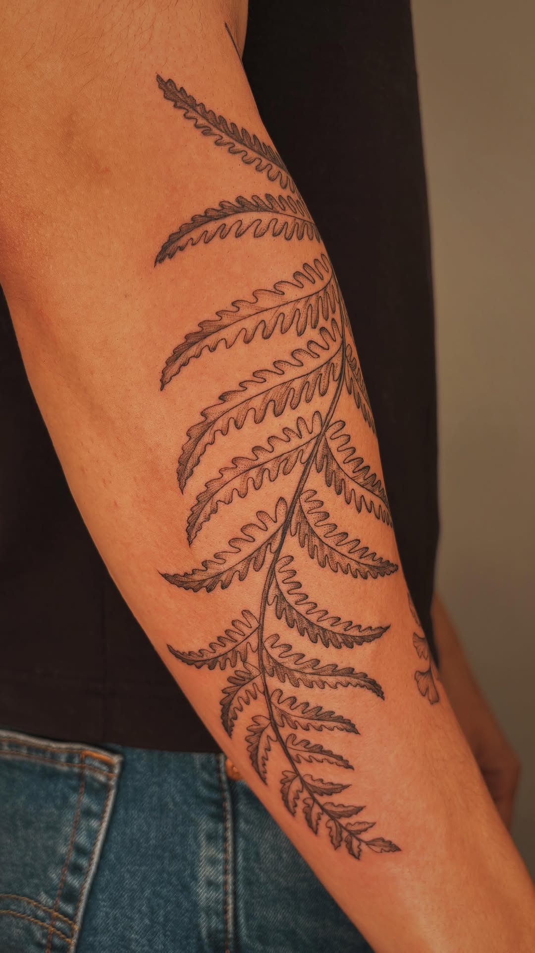 Elegant black fern frond wrap along forearm, bold linework