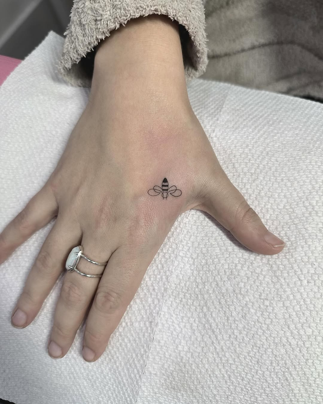 Tiny fine-line bee tattoo on the back of hand