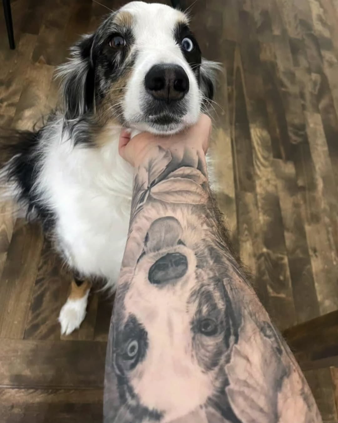 Hyper-realistic grayscale dog portrait on forearm, lifelike detail.