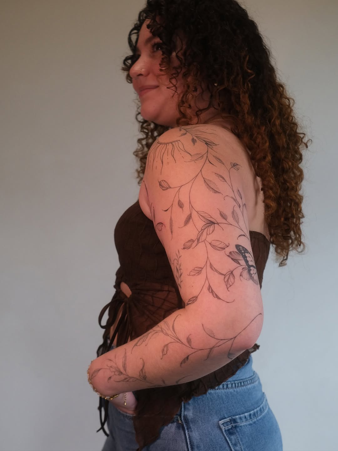 Delicate botanical vine and butterfly wrap forearm in fine-line florals