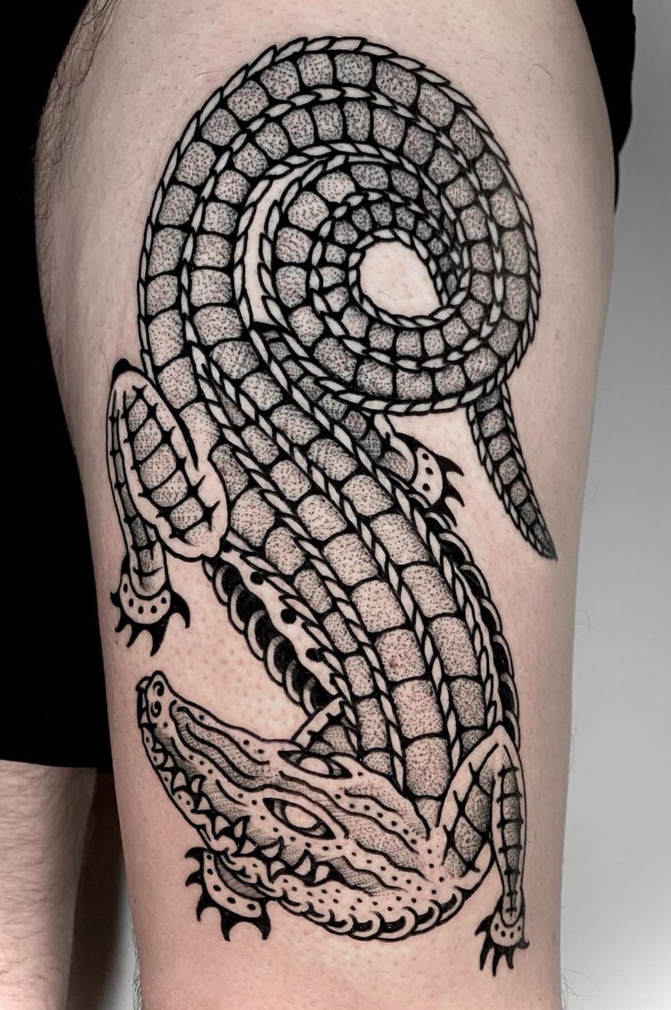 Coiled crocodile tattoo with bold outlines and dot shading