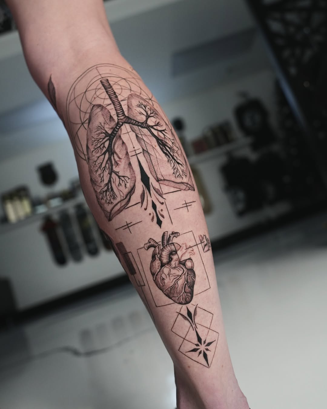 Intricate blackwork forearm piece: lungs, heart, geometric arcs.