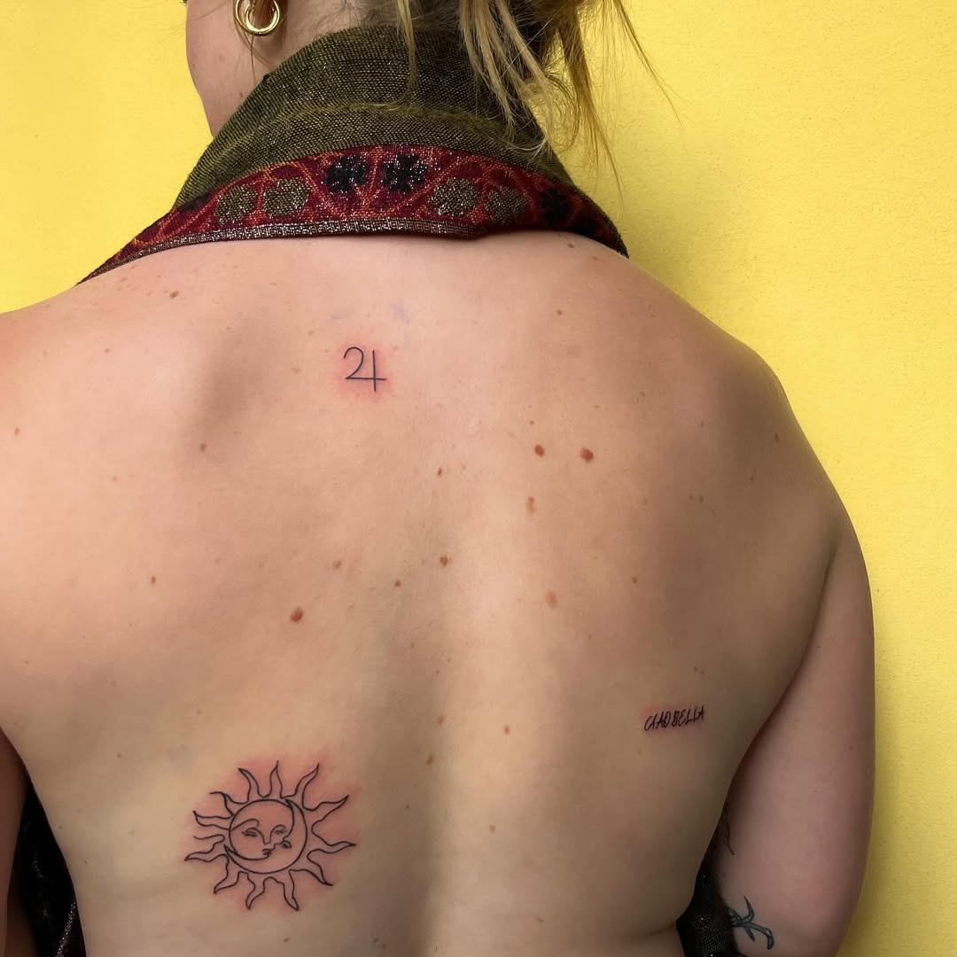 Three back tattoos: sun with a smiling face, 24, script.