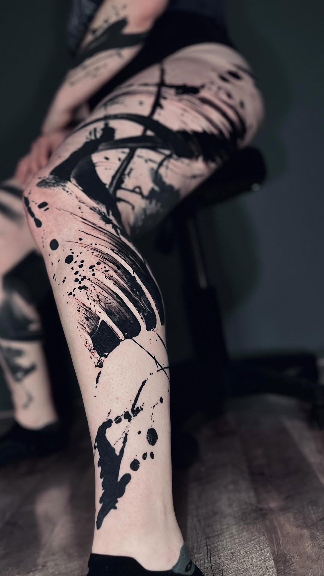 Bold abstract black brushstrokes dominate bare leg with splatters.