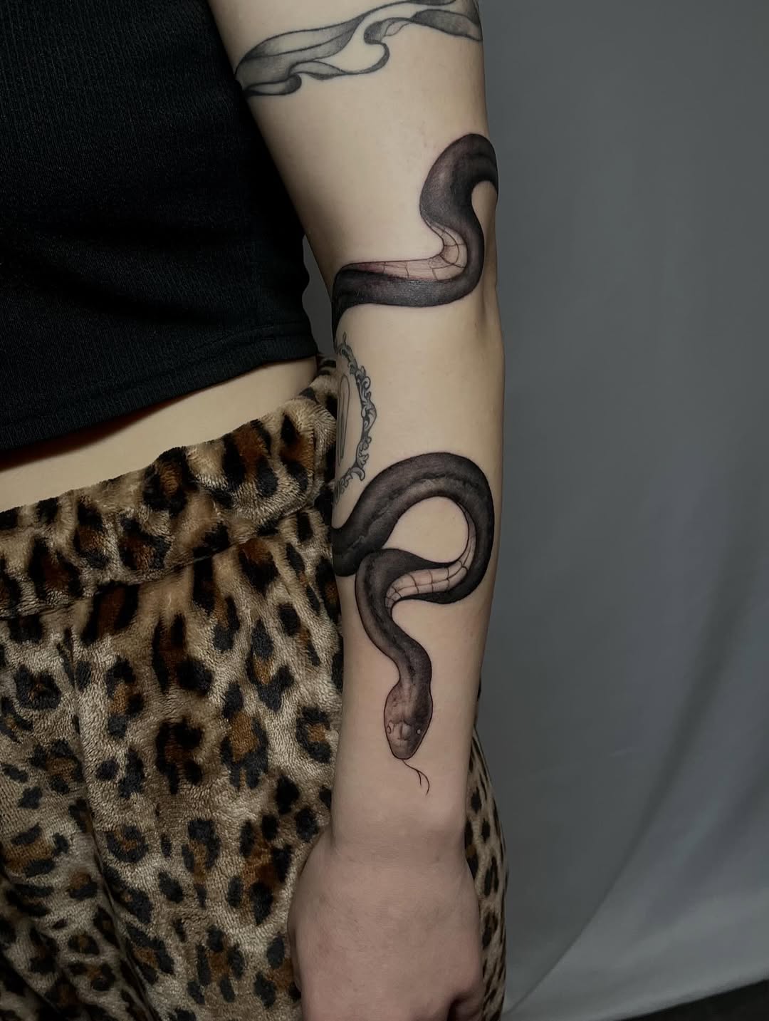 Sinuous black-gray snake coils along forearm in realism.