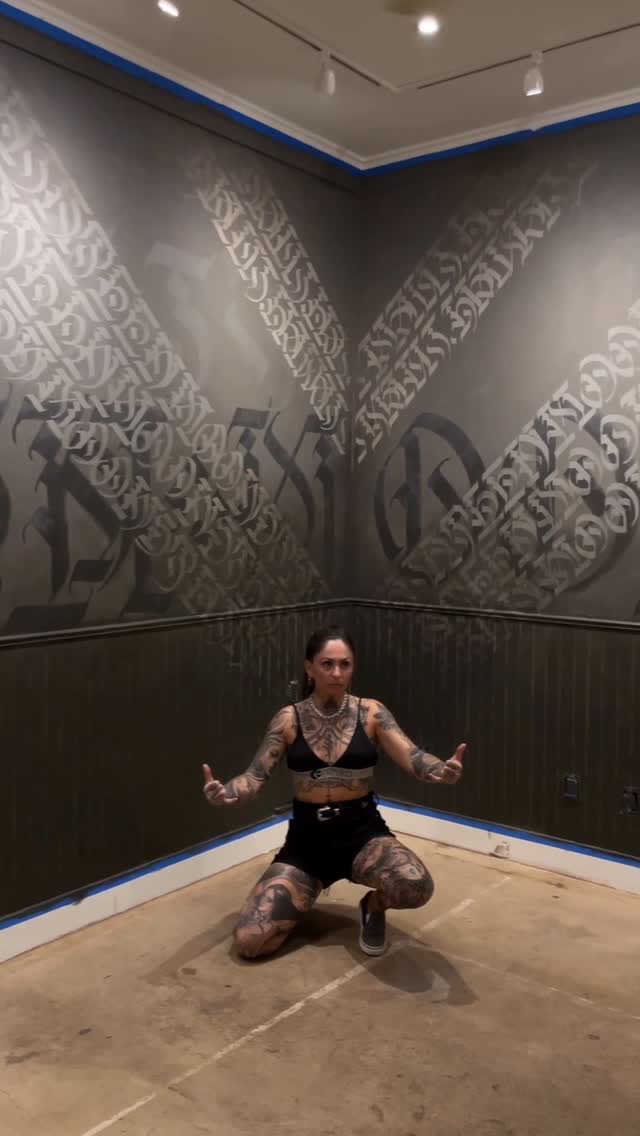 Kneeling, heavily tattooed woman with full-sleeve arms and thigh pieces.