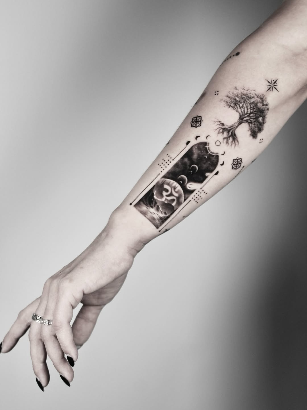 Intricate black-and-gray forearm tattoo featuring a tree and cosmic rectangle