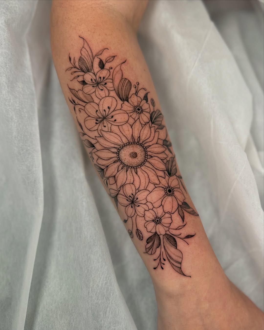 Intricate fine-line bouquet of mixed blossoms on forearm