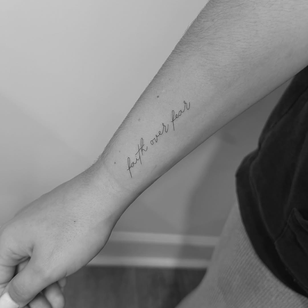 Elegant cursive script reading 'face the fear' on forearm.