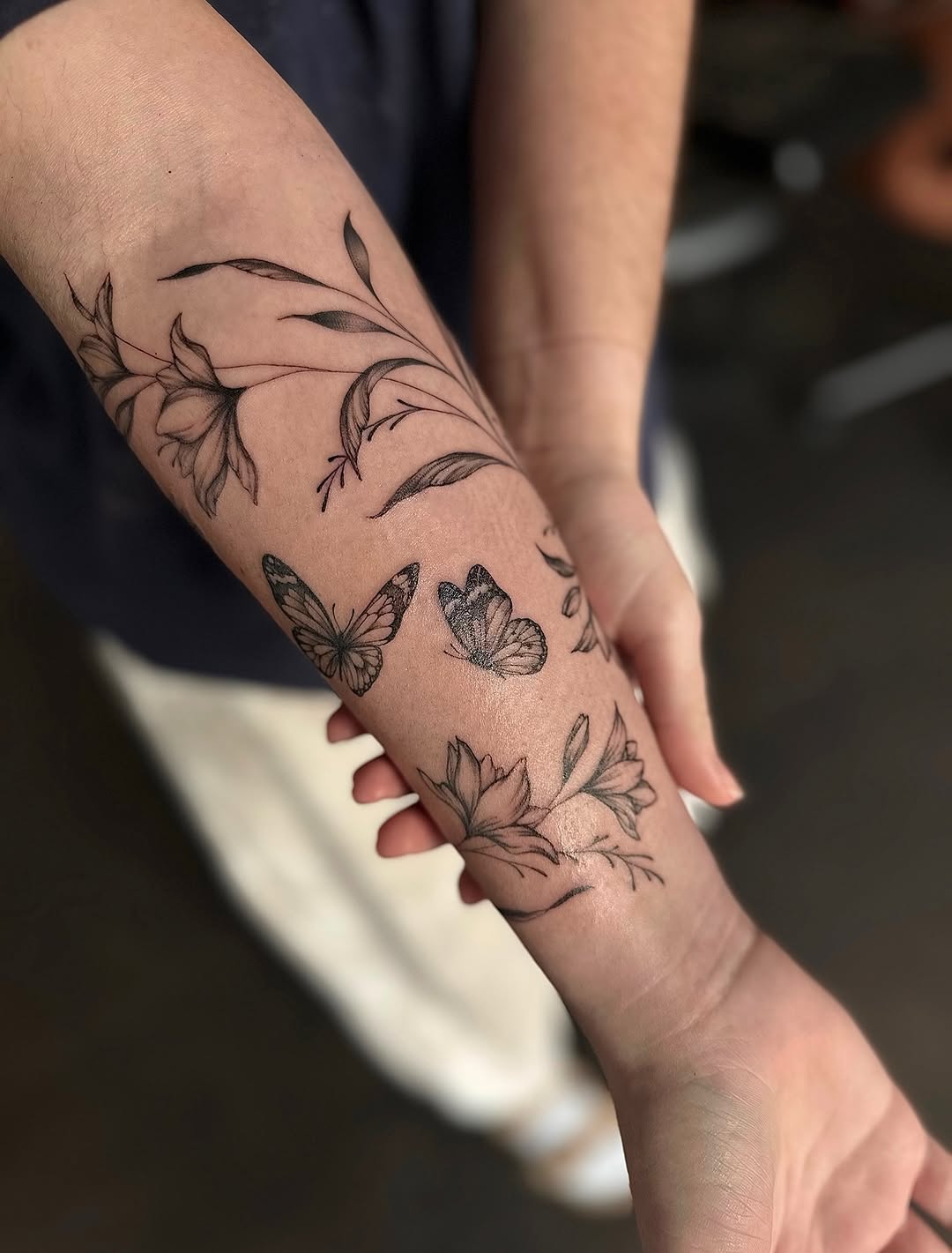 Delicate black-line butterflies entwined with floral vines on forearm.