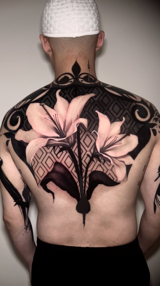 Monumental backpiece blending geometric blackwork with pale lilies.