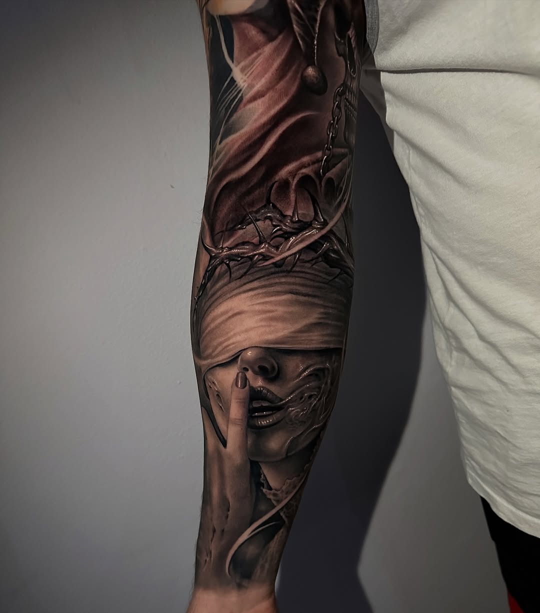 Hyper-realistic black-and-gray portrait on forearm, finger over lips