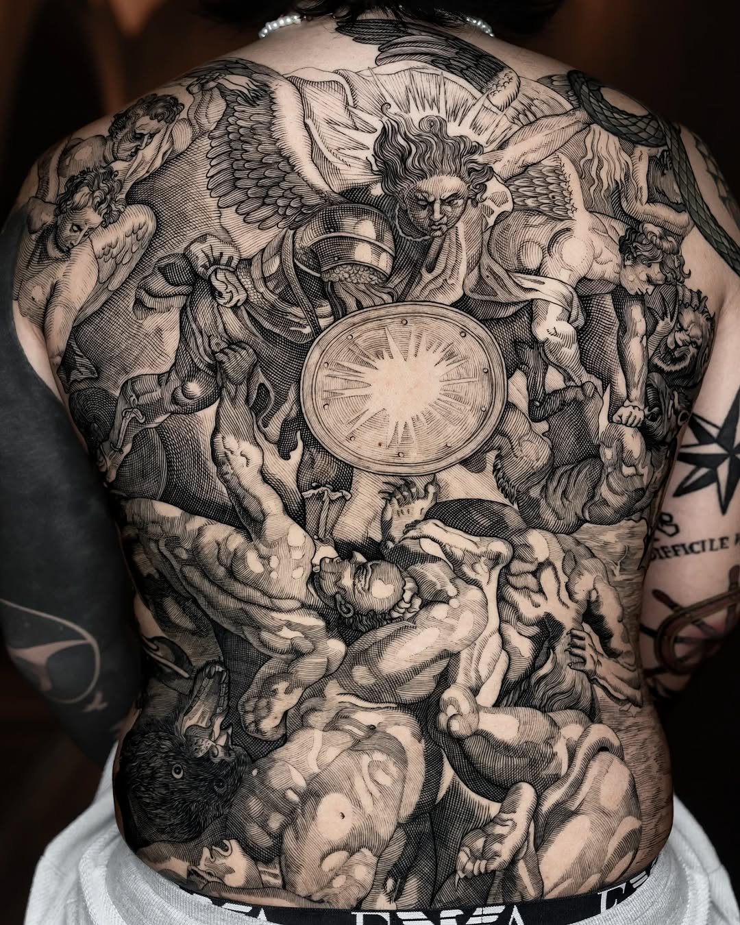 Epic blackwork back piece: winged figures clash in intricate linework.