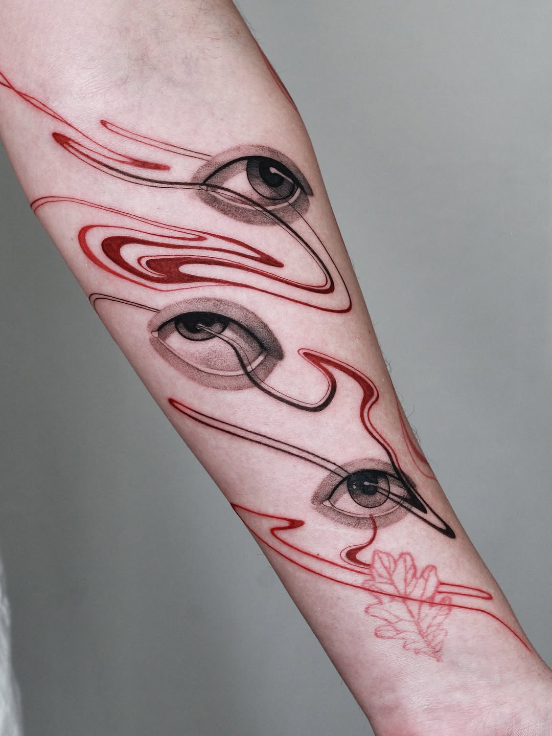 Surreal abstract forearm tattoo with floating eyes and red swirls