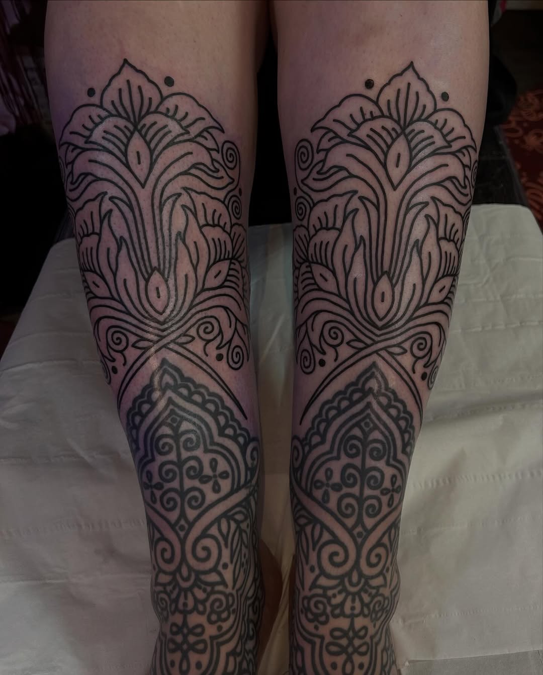 Intricate blackwork ornamental floral leg tattoos, mirrored.