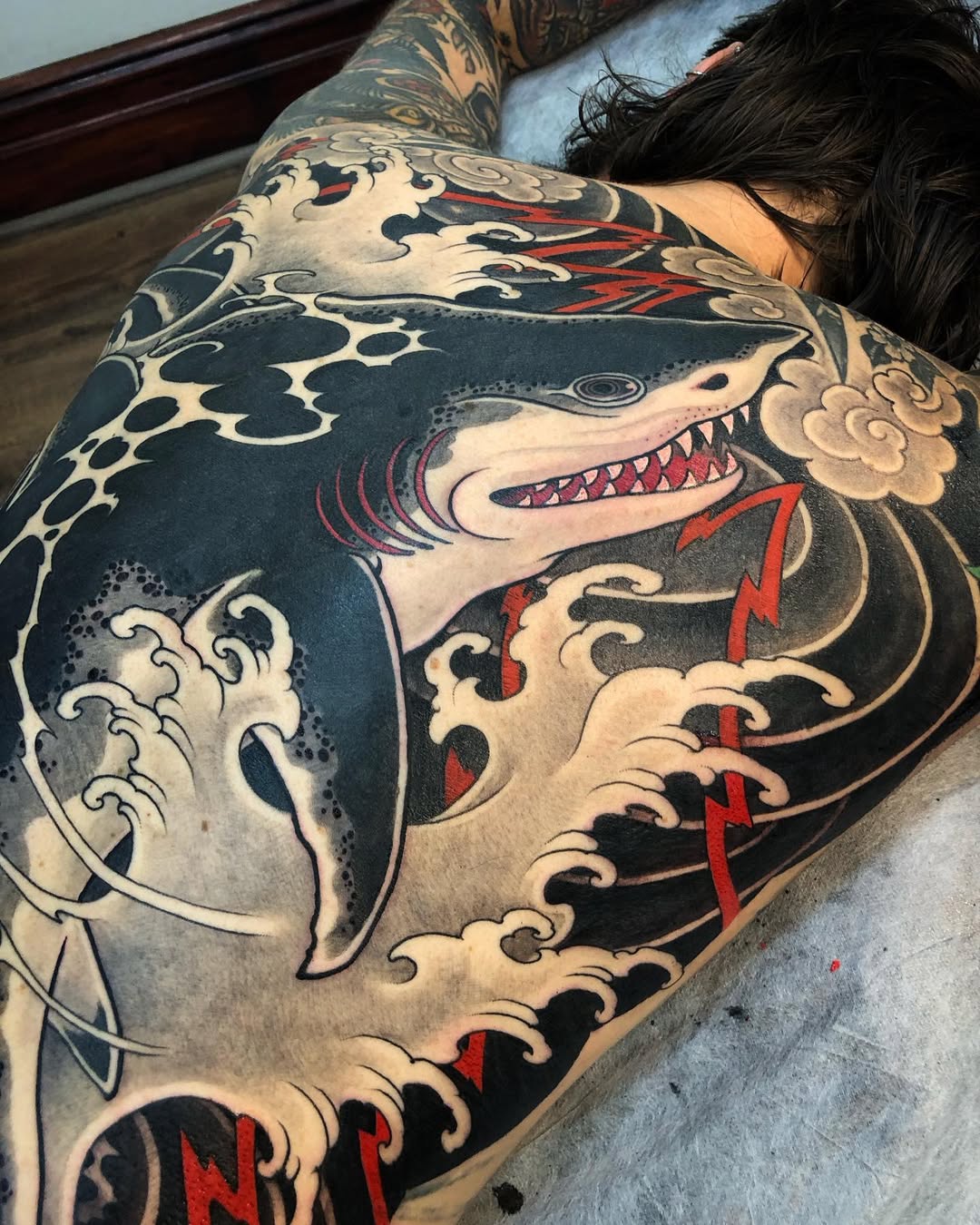 Bold Japanese shark tattoo amid roaring waves, blackwork with red accents.