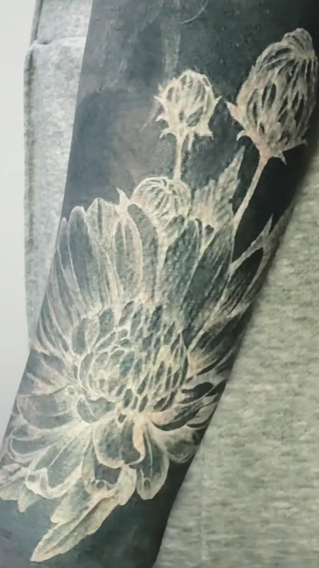 Intricate white-ink chrysanthemum blooms on dark forearm
