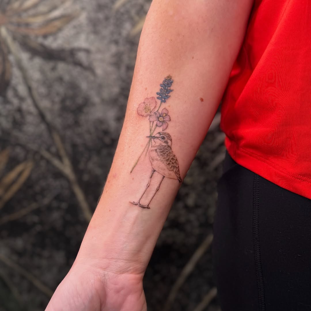 Delicate fine-line bird with pastel flowers on forearm.