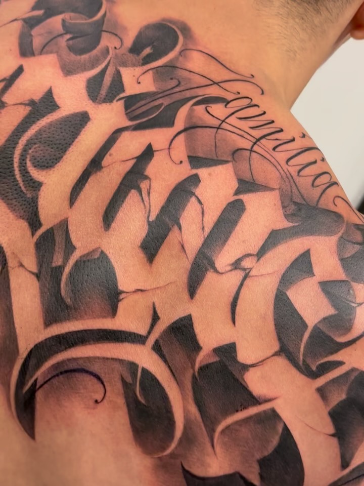 Bold blackwork geometry with flowing script on shoulder.