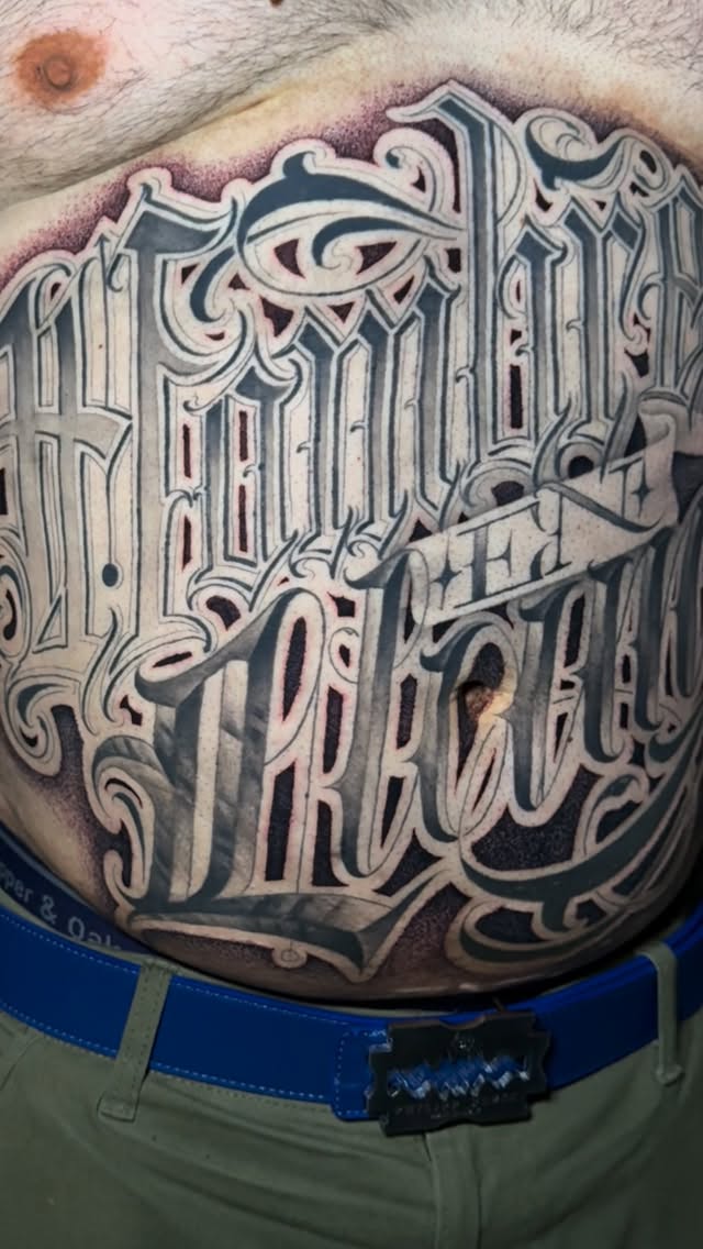 Elaborate blackletter script tattoo across back with ornate shading