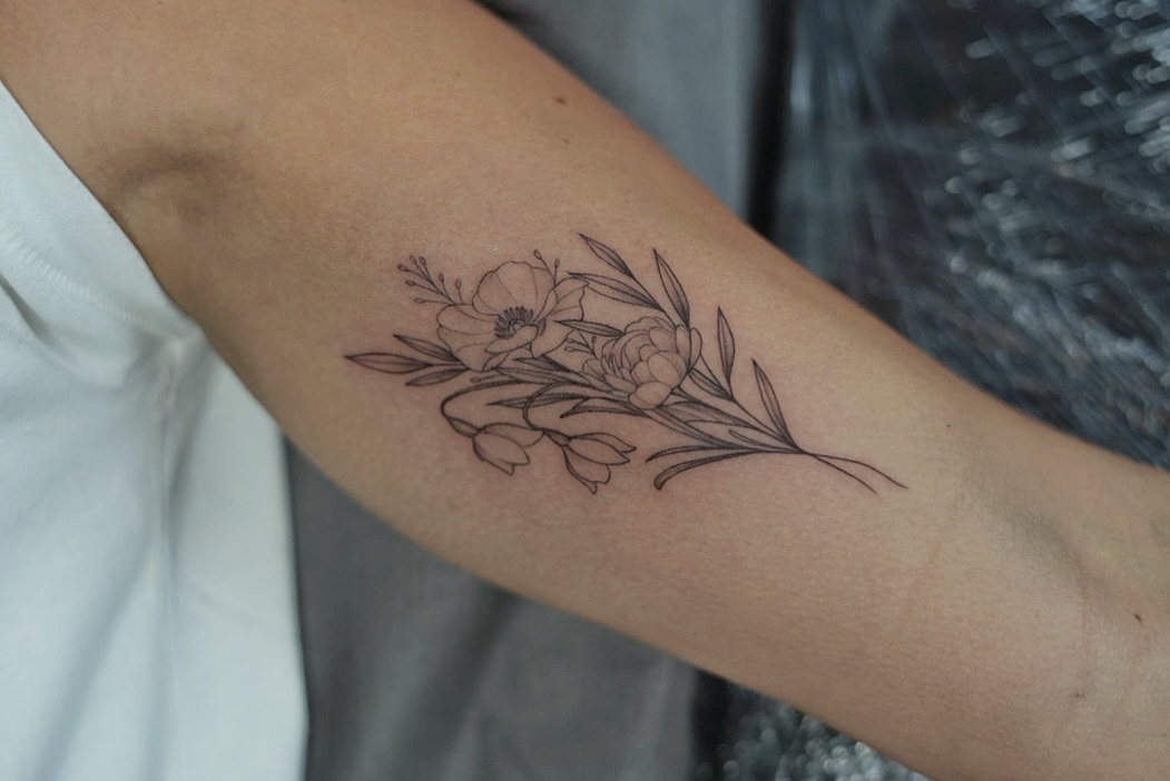 Delicate fineline birth-flower bouquet on the forearm