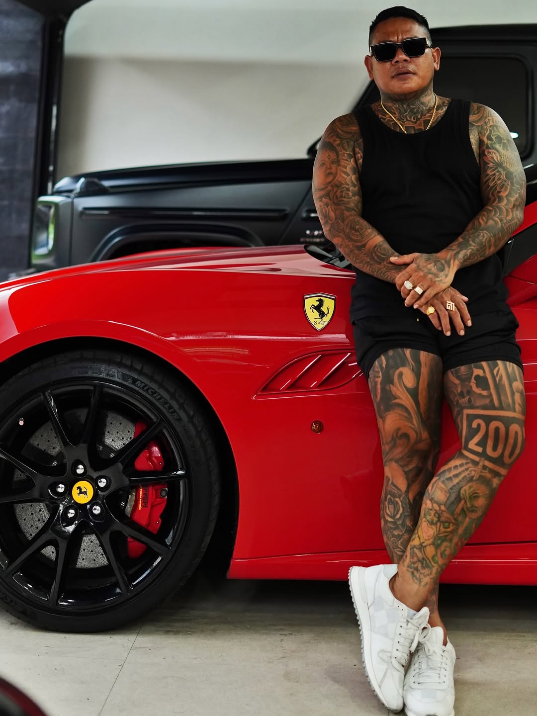Tattooed man leaning on red Ferrari, bold full-sleeve