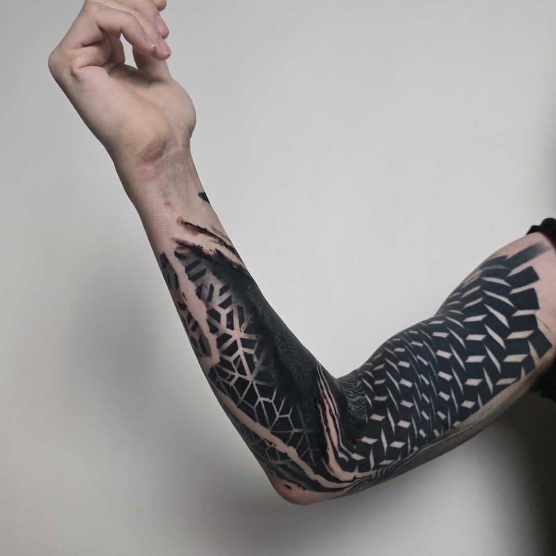 Monochrome geometric blackwork sleeve with negative-space tessellations.