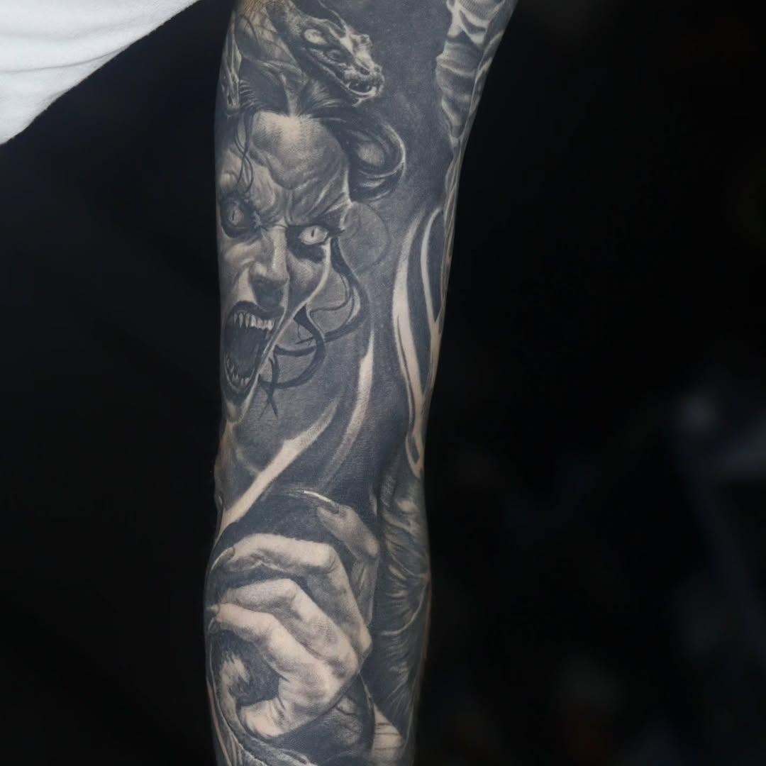 Grayscale demon portrait with snarling maw on forearm.