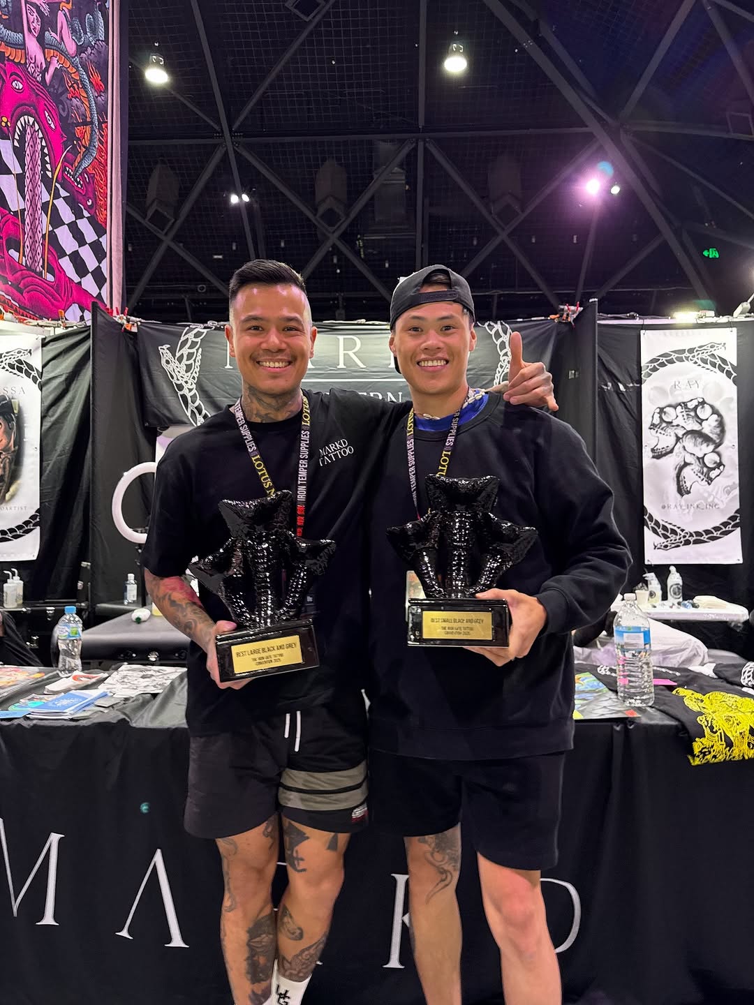 Two tattoo artists celebrate at convention with black-and-gray trophies