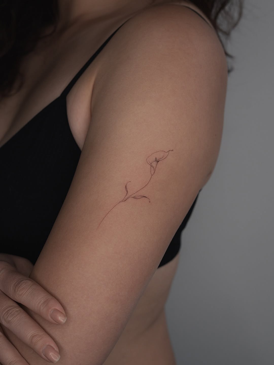 Delicate fineline calla lily tattoo on the upper arm.