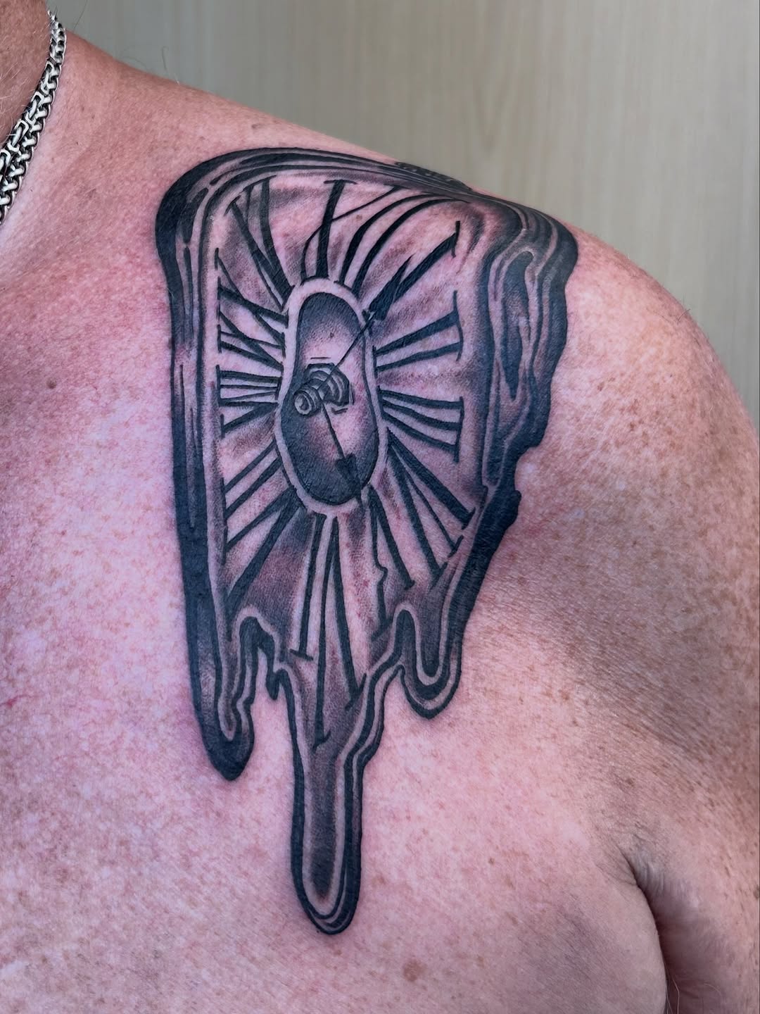 Melting clock tattoo with dripping, bold black shading.