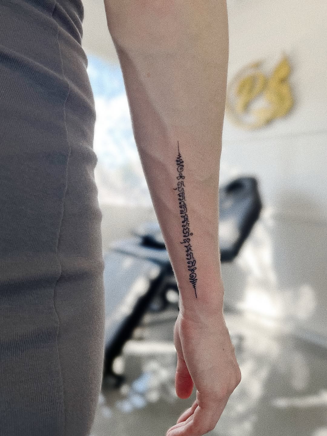 Slim vertical Sak Yant script along forearm, precise blackline