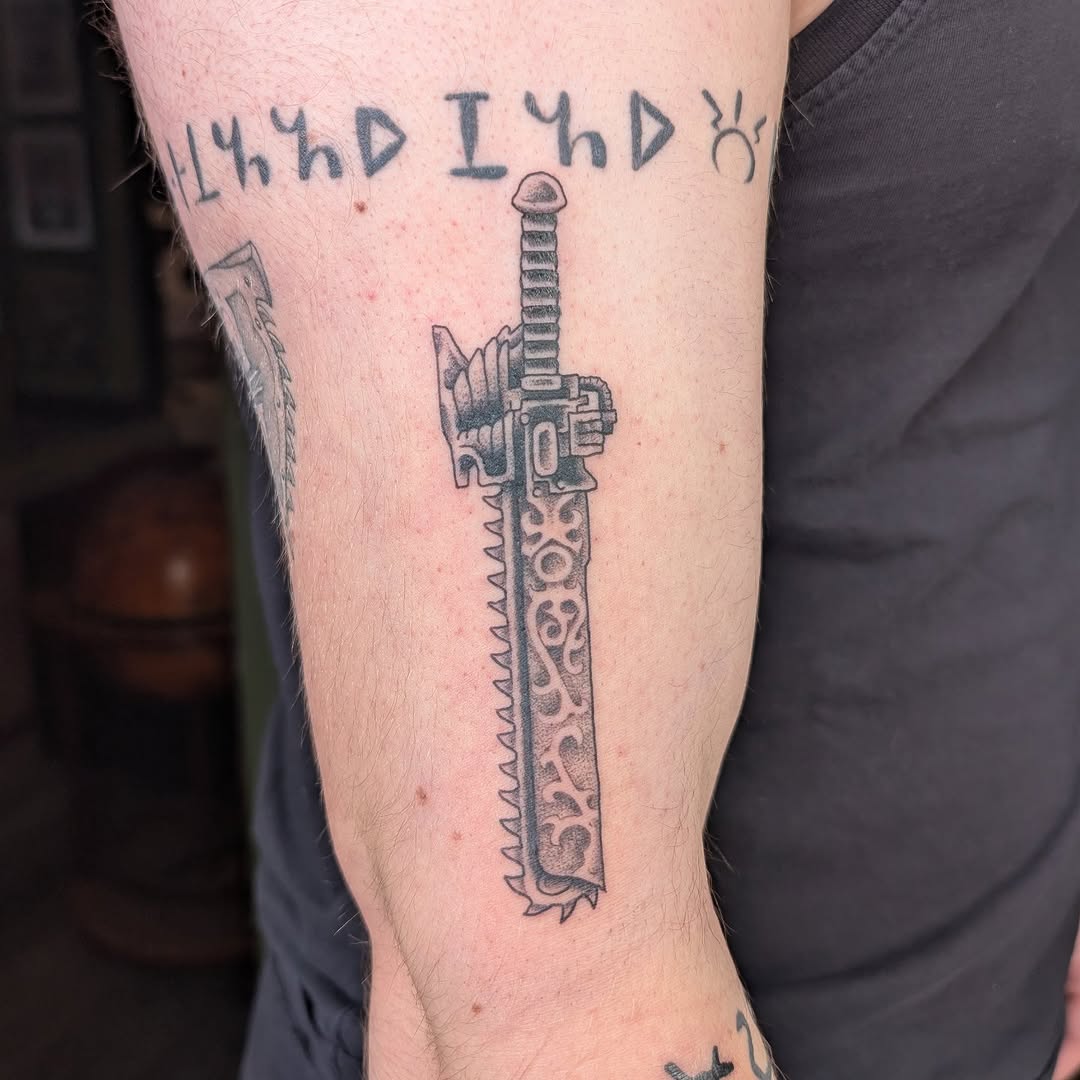 Warhammer-style chainsword tattoo with jagged teeth and hilt