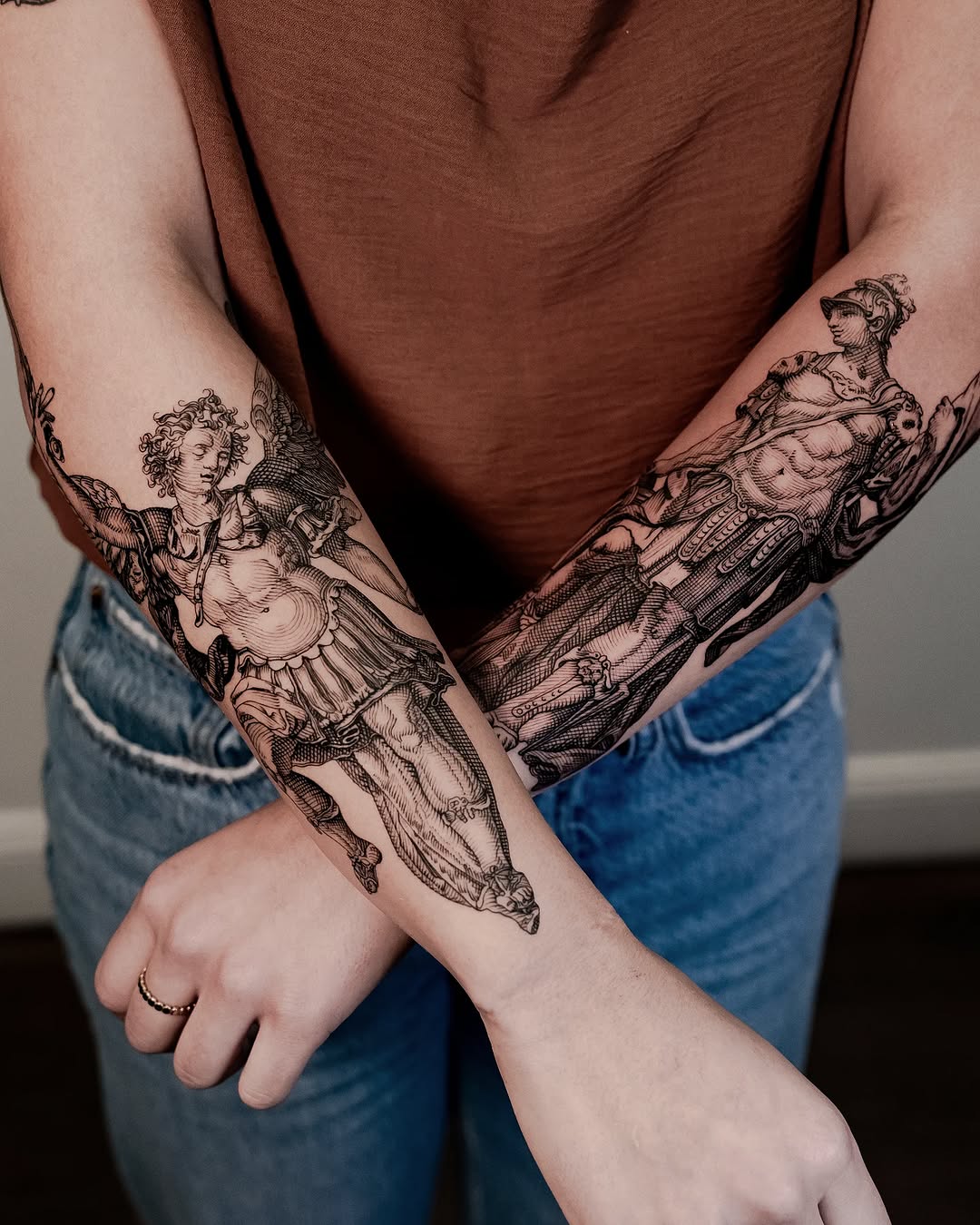 Intricate etched saints in armor, blackwork forearms.