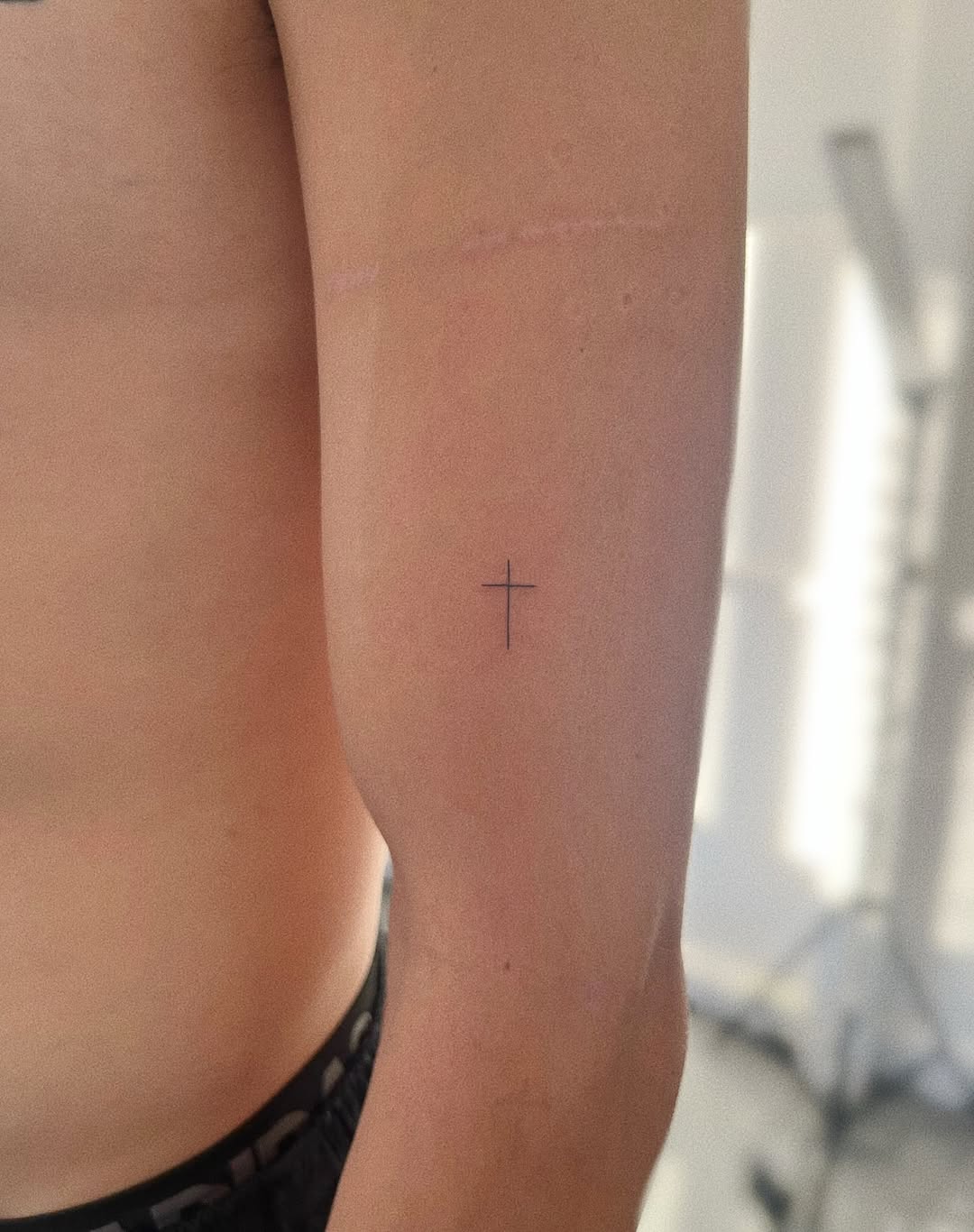 Minimalist fine-line cross on inner forearm.