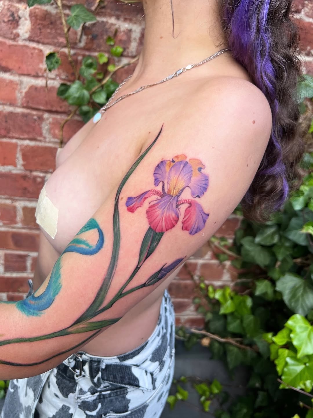 Vibrant iris tattoo with watercolor stems on bare shoulder