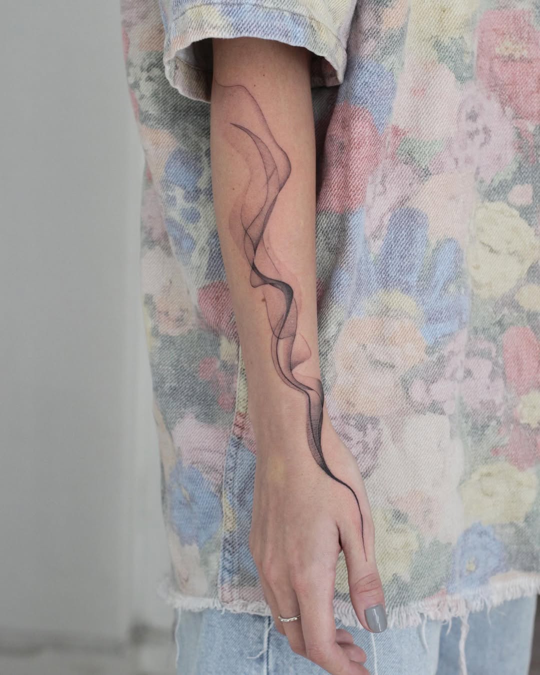 Slim wispy black-line, abstract smoke tattoo along forearm.