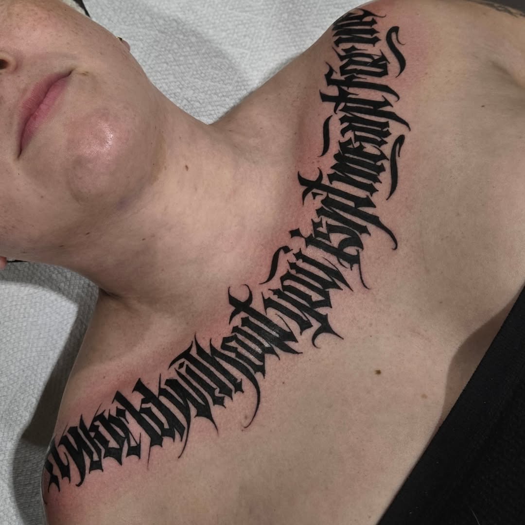 Bold blackletter script arcs along collarbone and shoulder
