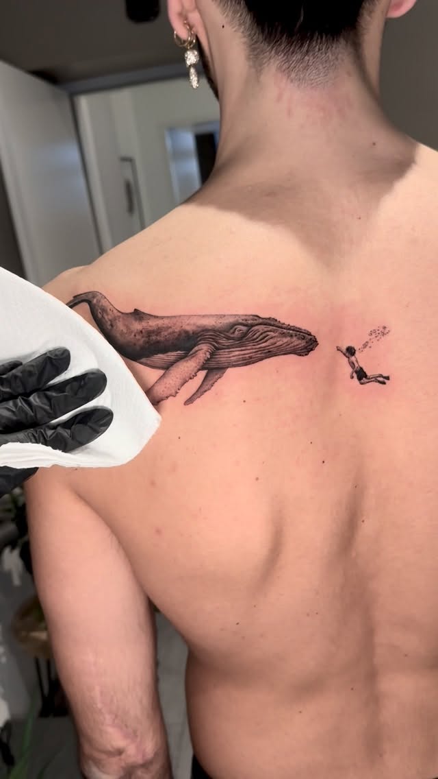 Delicate fineline whale spans shoulder with a lone diver.