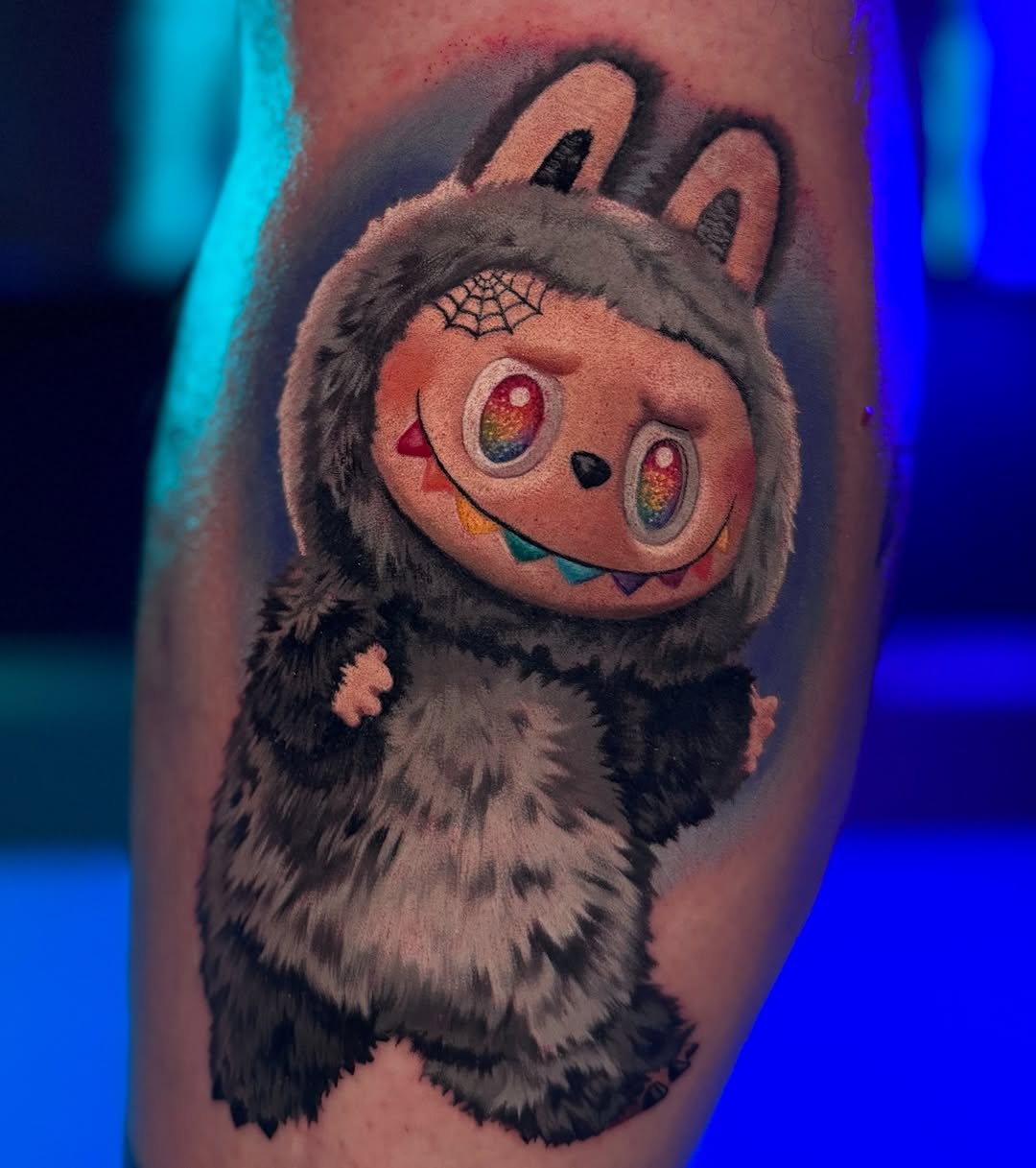 Chibi Labubu creature tattoo with rainbow eyes.