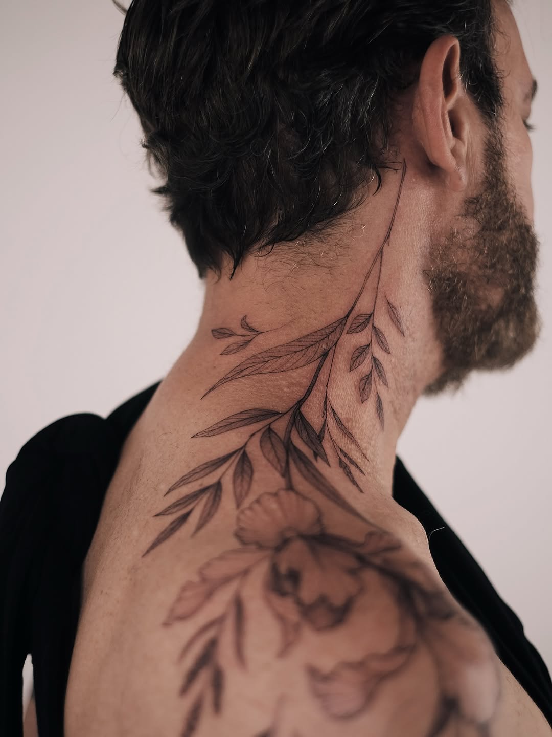 Delicate neck botanical tattoo with fine-line leaves and bloom.
