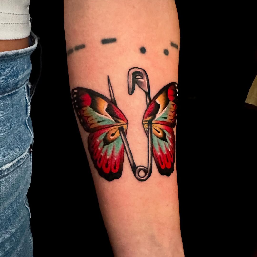 Vivid butterfly wings flanking a bold safety-pin motif.