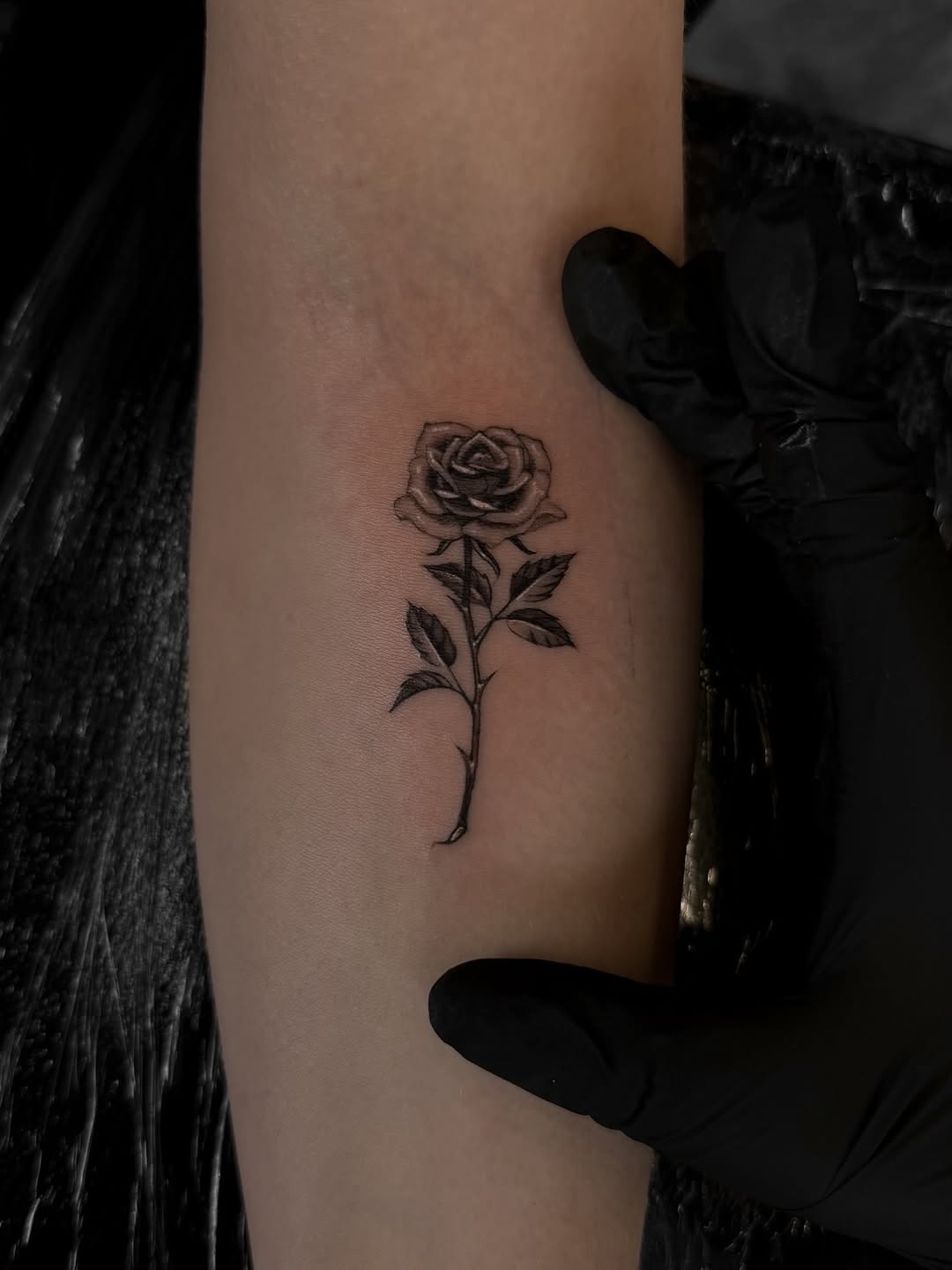 Delicate fine-line rose on inner forearm, minimalist bloom.